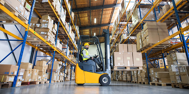 A warehouse employee operates a forklift in a warehouse filled with pallet racks