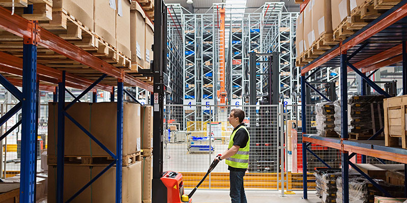A warehouse worker working in a modern automated warehouse full of pallet racks and stackers