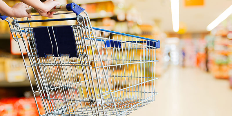 A woman pushes an empty shopping cart through a supermarket while her hands and cart are focused