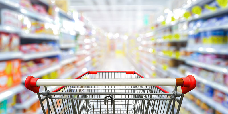 The background aisle of a supermarket is distorted with the red shopping cart in the foreground